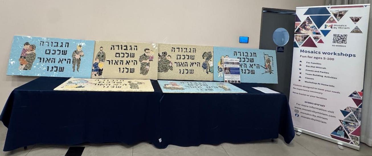 A row of mosaic murals next to a Mosaics by Miriam workshops banner