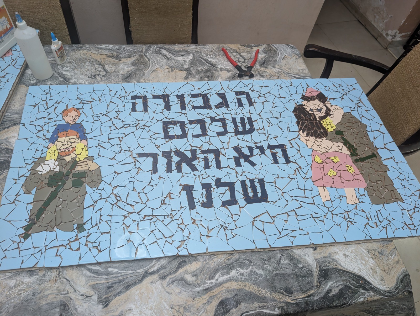 Handmade mosaic mural of a soldier carrying a child and a woman embracing a soldier, with Hebrew lettering
