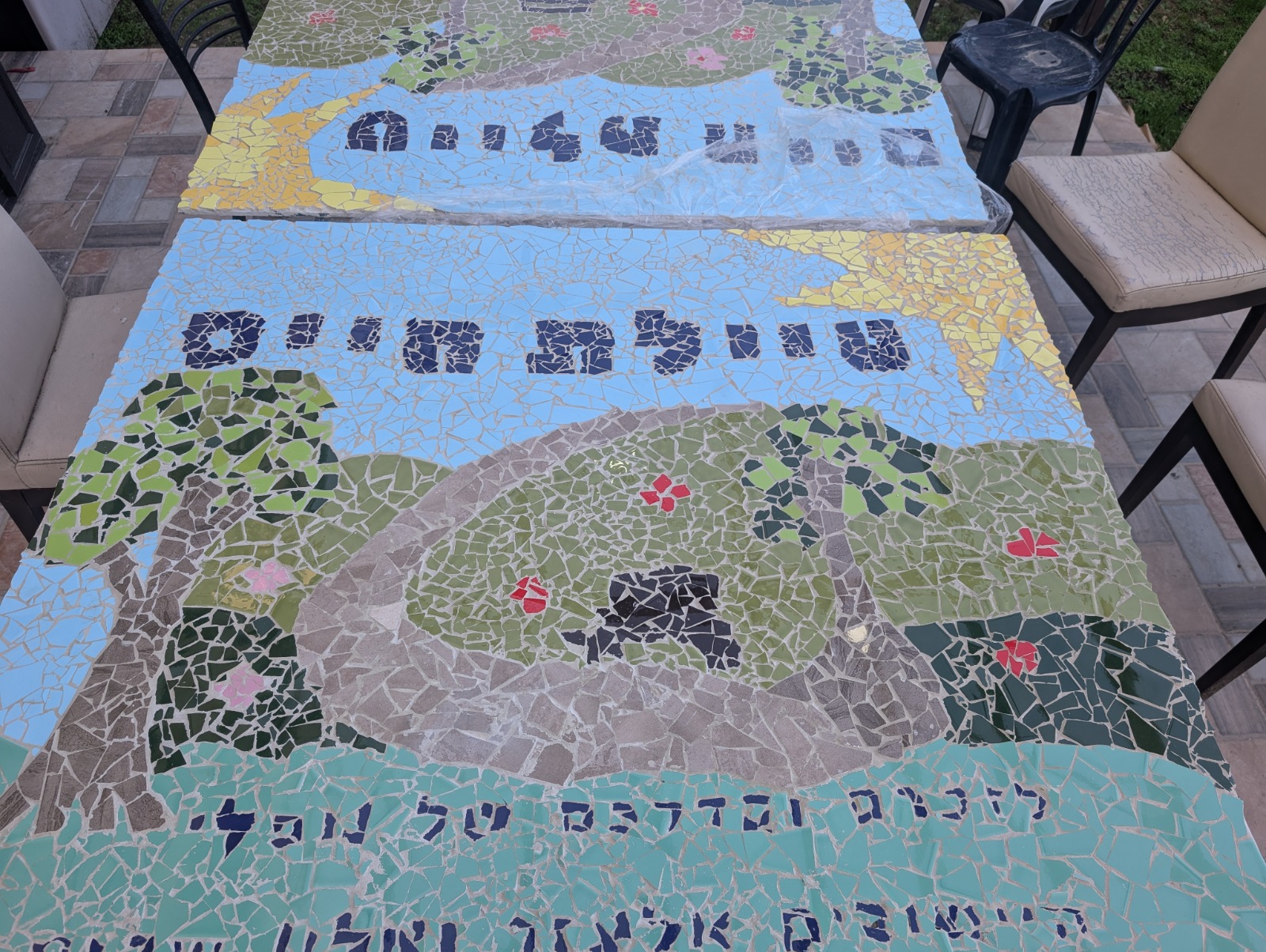Handmade mosaic of a sunlit landscape with paths, trees and Hebrew lettering, slated for display at Tayelet Chaim between Elazar and Alon Shevut